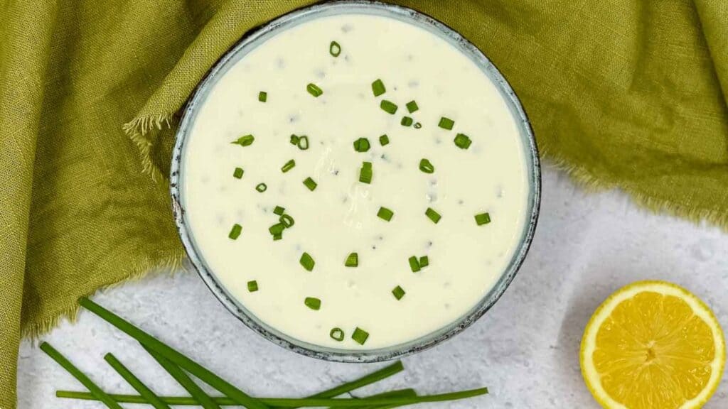 Sour cream and chives dressing in a bowl with chives and lemon around it.