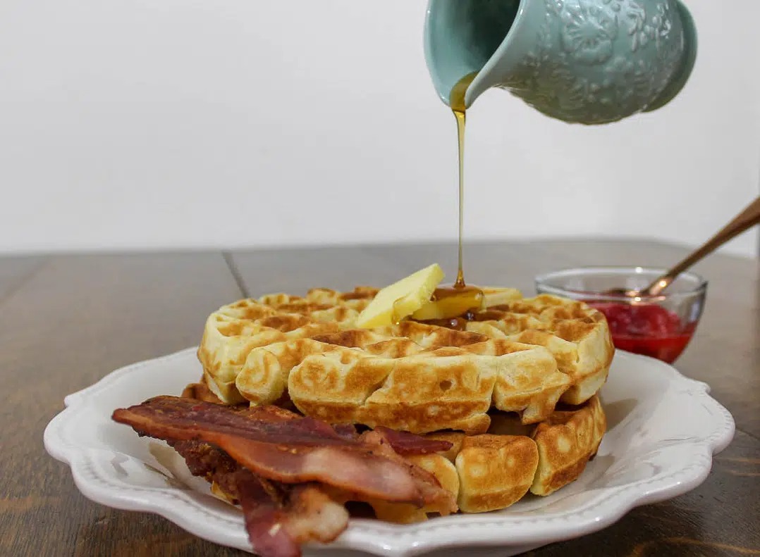 Pouring syrup over a stack of waffles.