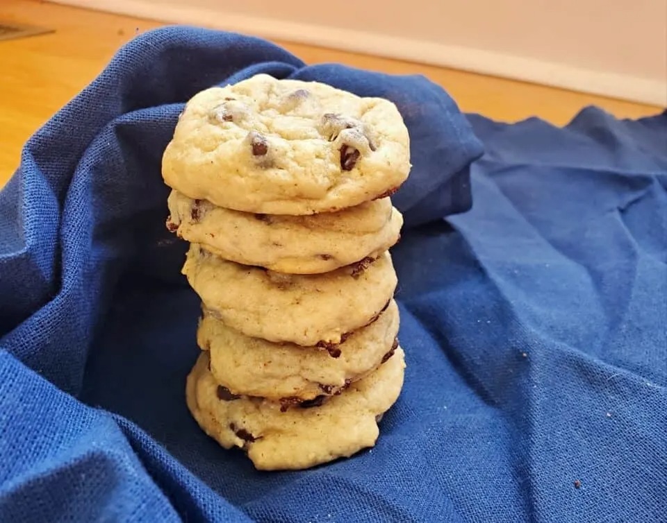 Stack of sourdough chocolate chip cookies sits on a wood board with a blue cloth artfully surrounding the stack.