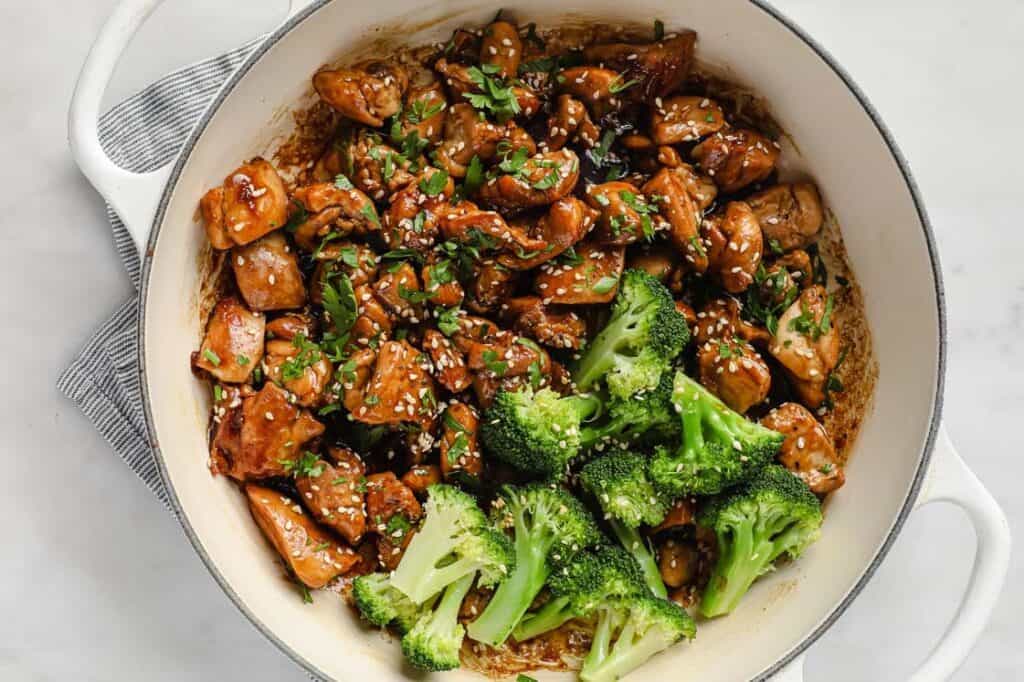 Sticky sauce chicken, broccoli, and sesame seeds in a pot.