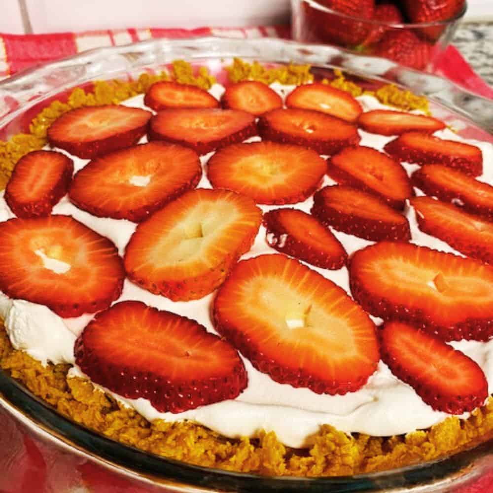 Close up of whole strawberry cream pie with bowl of strawberries in background