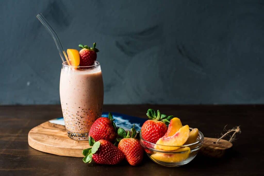 A strawberry peach smoothie on a wood board next to strawberries and peaches with text overlay for social media.