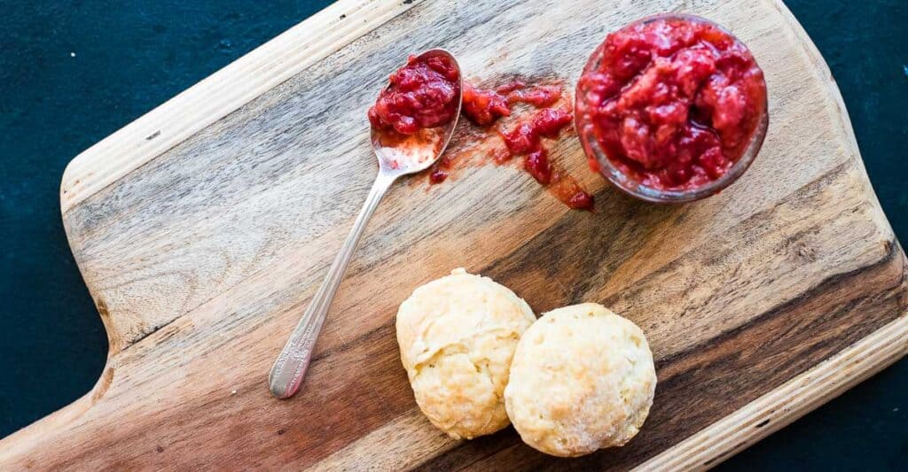 Biscuits and strawberry rhubarb jam in a jar on a cutting board.