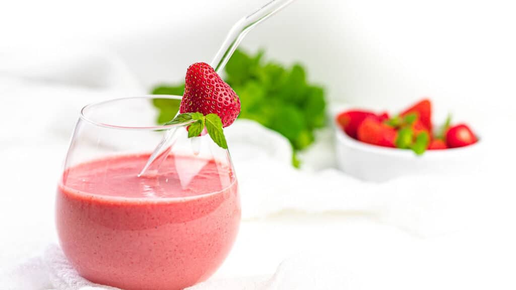Strawberry Mint Keto Smoothie inside a glass with straw and fresh strawberry.