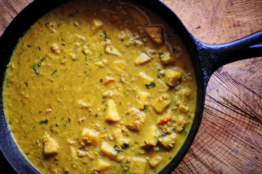 A large skillet filled with a yellow curry resting on a wooden table.