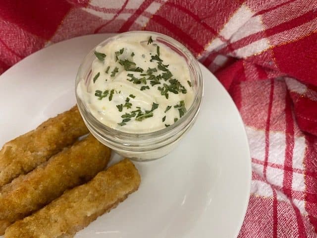 Tartar sauce in clear jar on plate of fish sticks