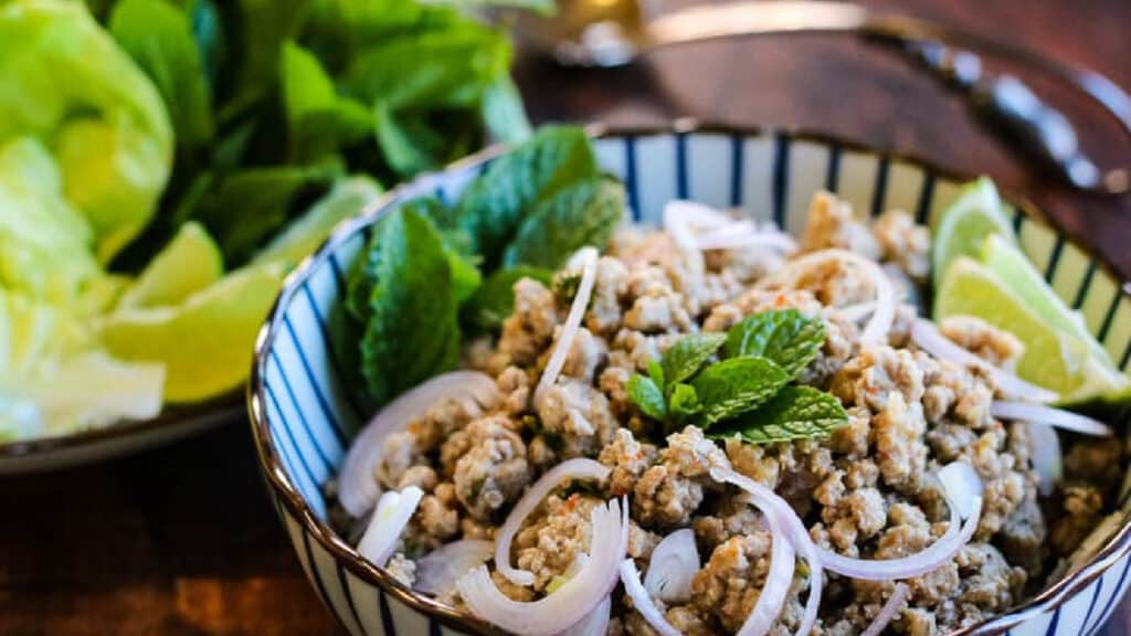 Low angle shot of a striped bowl filled with Thai larb salad garnished with shallot slices.