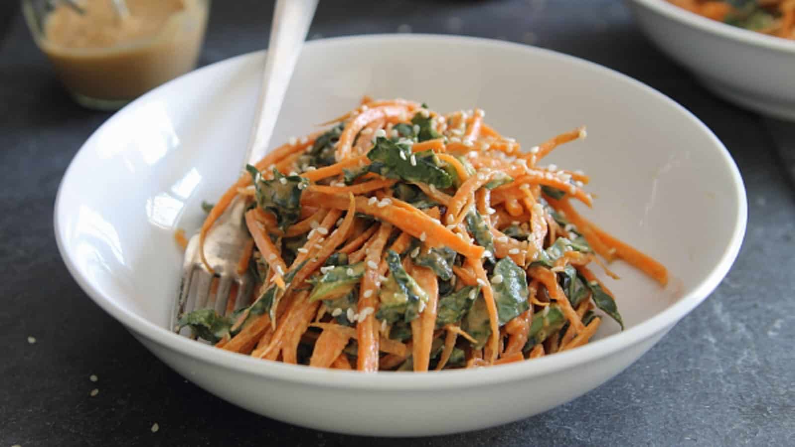 Spicy Thai carrot and kale salad in a white bowl with a fork.