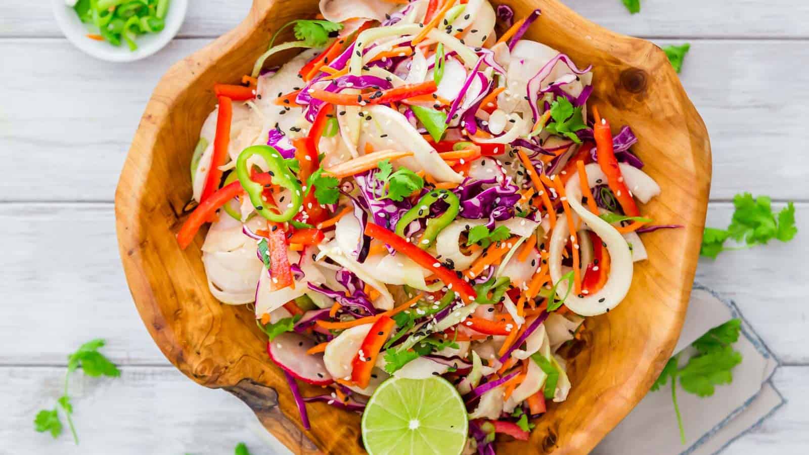 Thai kohlrabi noodle salad in a wooden bowl with limes.