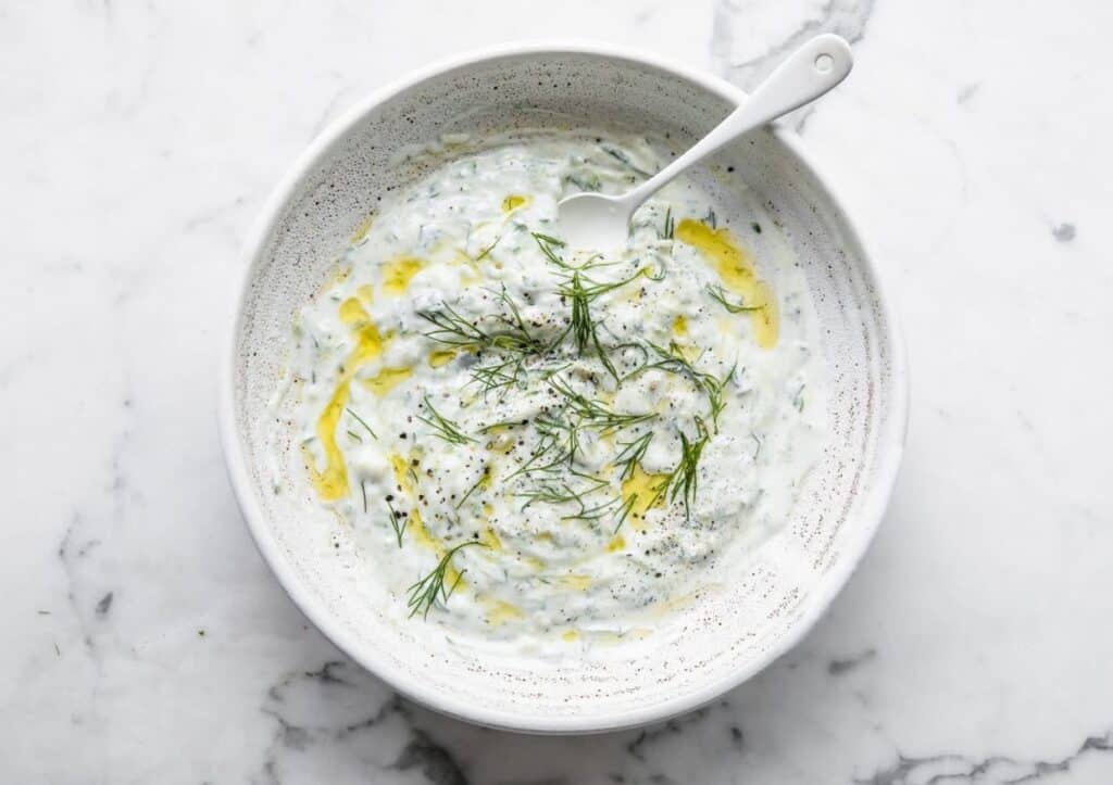 A garnished bowl of tzatziki with a spoon.