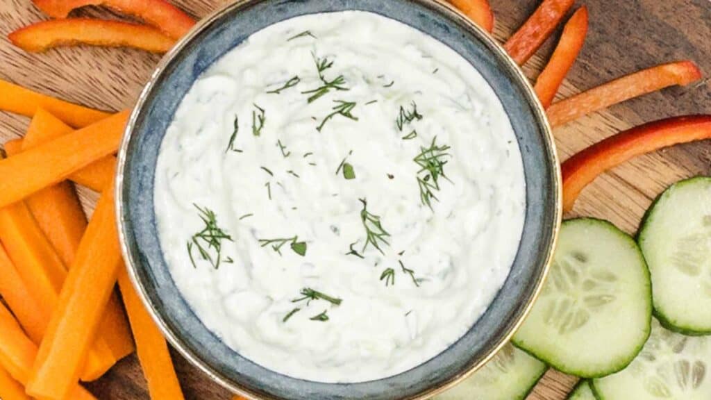 Tzatziki in a bowl with sliced veggies surrounding it.