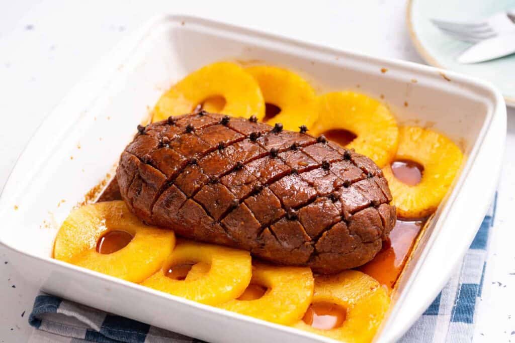 Close up of vegan ham roast in a white baking dish, on top of a blue and white stripe napkin