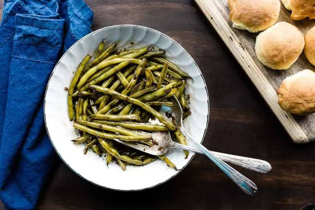 Overhead shot of worcestershire green beans in a white serving bowl next to a blue towel.