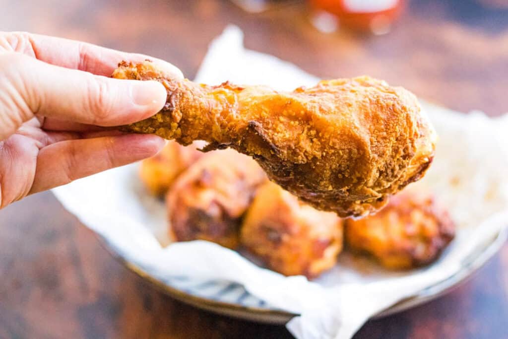 A hand holding a crispy fried chicken drumstick.