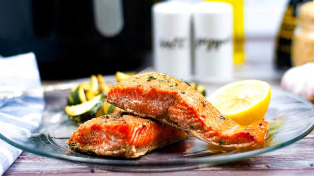 salmon on a plate with sauteed zucchini and a lemon wedge.