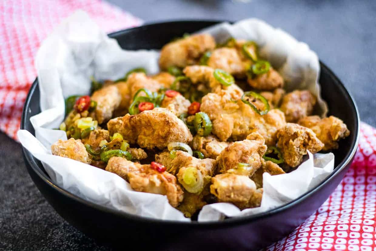 fried salt and pepper chicken in a black bowl lined with parchment paper.