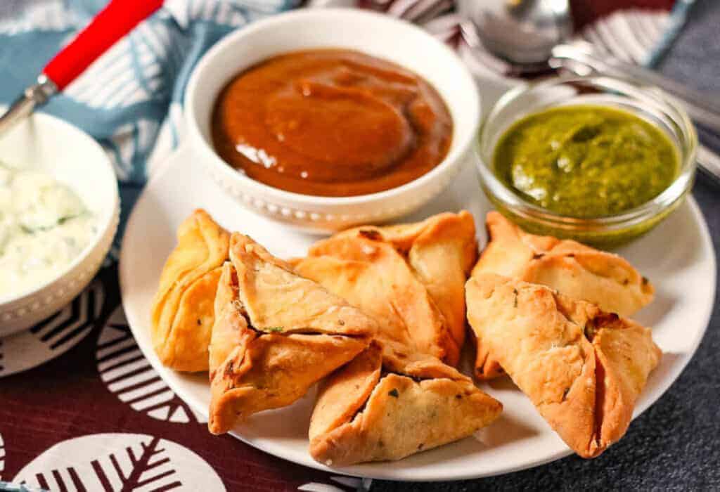 Plate of samosaas with tamarind chutney and cilantro mint chutney.