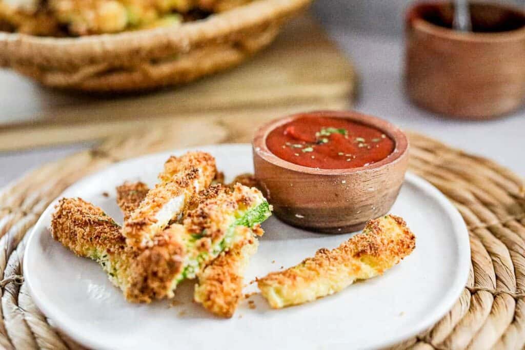 Zucchini fries on a plate with spicy ketchup for dipping.