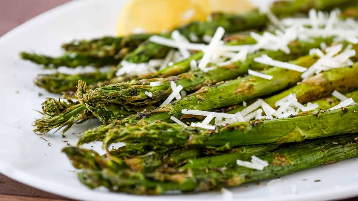 Roasted asparagus topped with parmesan with a lemon wedge in the background.