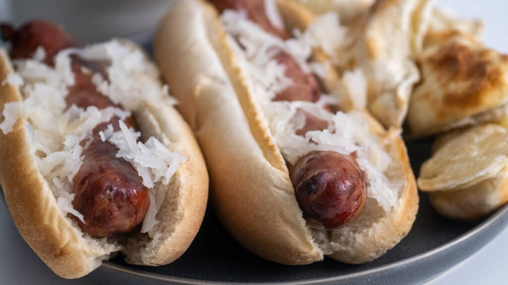 two brats on a plate in buns topped with sauerkraut.