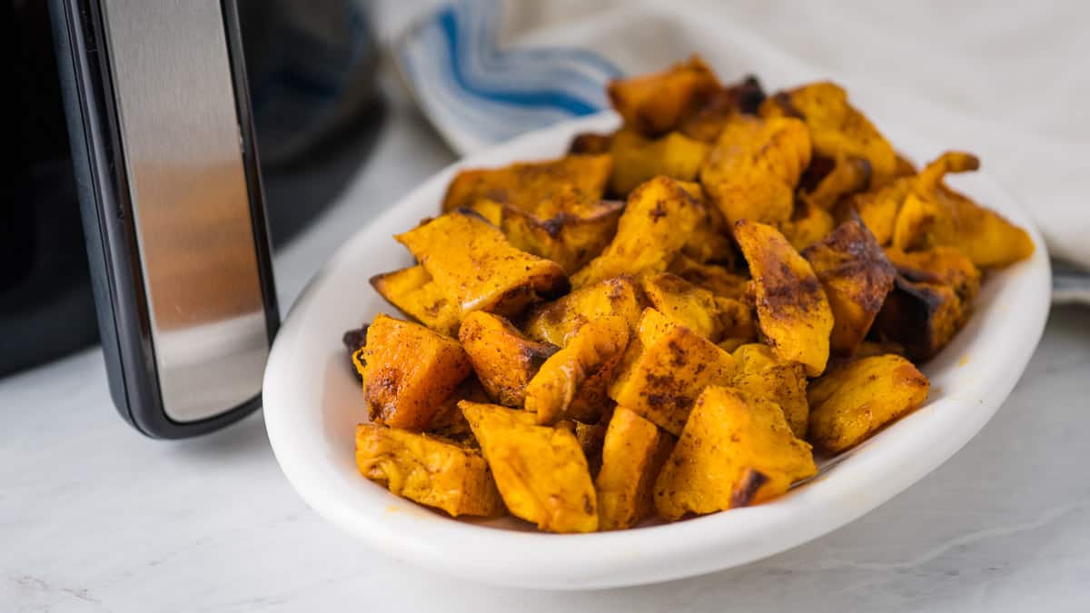 Plate of butternut squash in front of an air fryer with a blue napkin in the background.