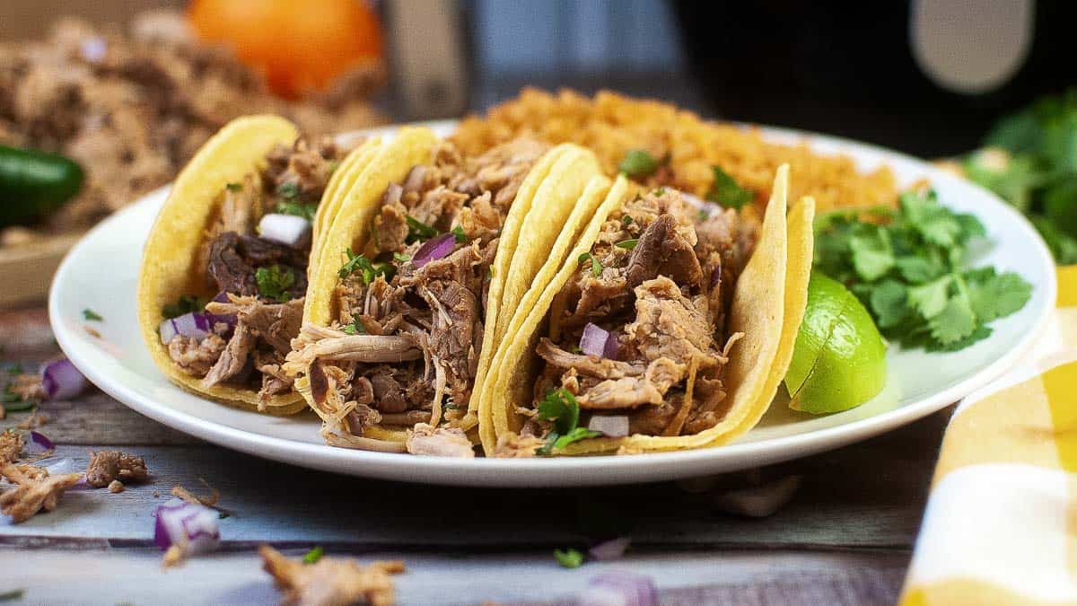 Three tacos made from air fryer carnitas on a plate with onions, cilantro and lime.
