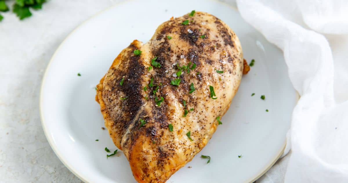 Juicy Air Fryer Boneless Skinless Chicken Breast on a white plate with parsley, onions, and tomatoes.