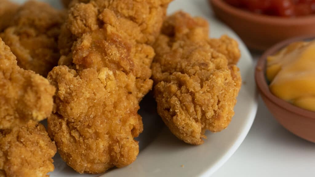 chicken tenders on a plate with dipping sauces in the background.