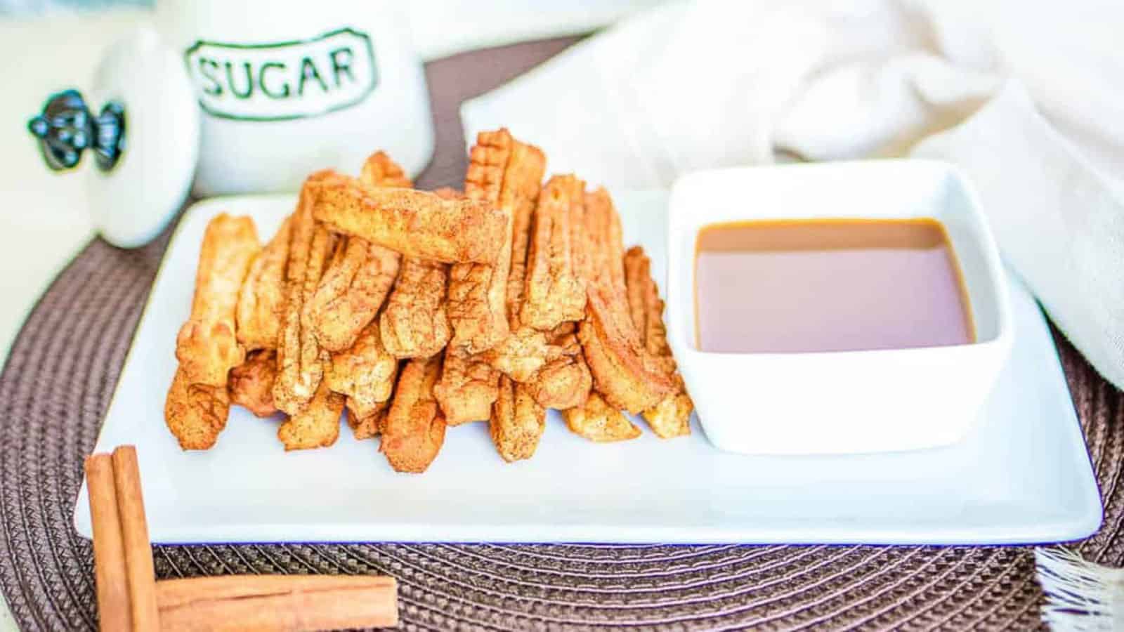 Churros on a white plate with a bowl of caramel dipping sauce on the side.