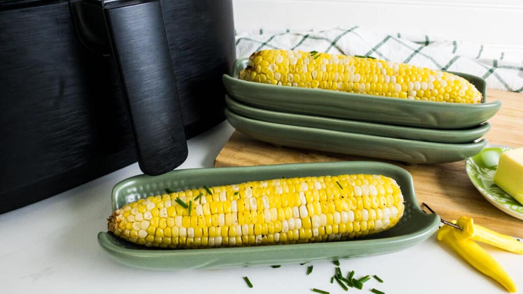 corn on the cob in a green corn dish in front of an air fryer.