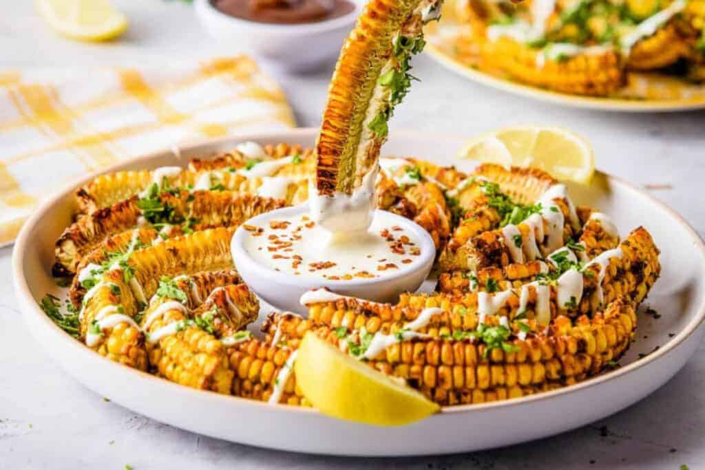 Corn ribs on a plate being dipped into creamy sauce.