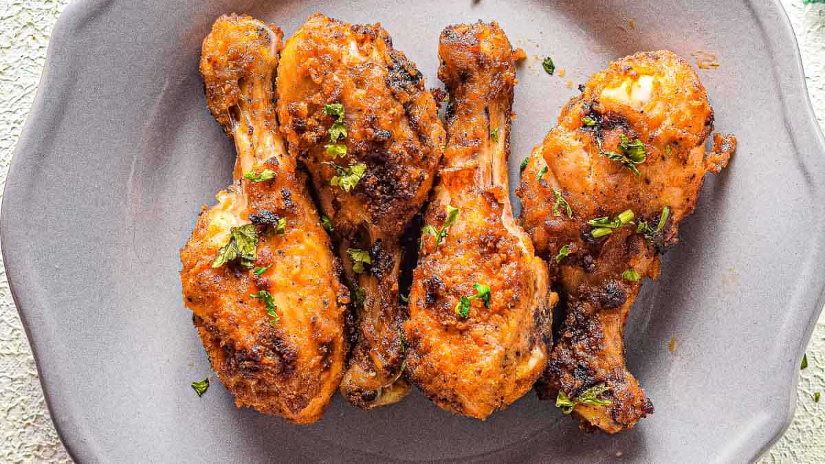 Four chicken drumsticks with parsley on a plate.