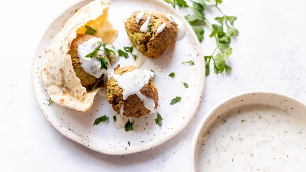 A white plate filled with falafel and fresh green herbs.