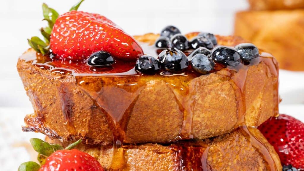 French toast topped with strawberries and blueberries and drizzled with syrup.