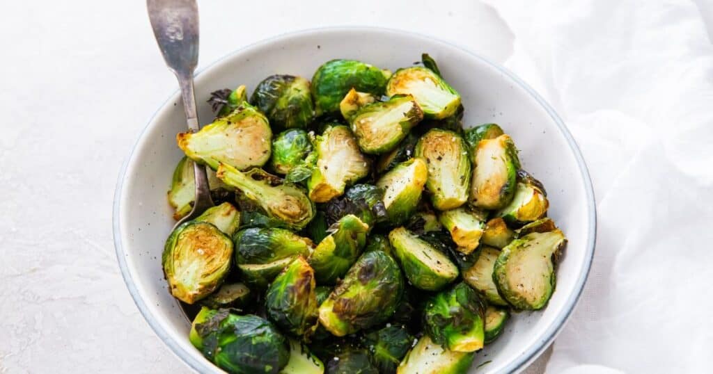 A bowl of low carb roasted brussels sprouts on a white surface with a spoon.