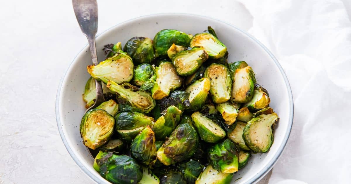 Brussel Sprouts in a white bowl with a spoon.