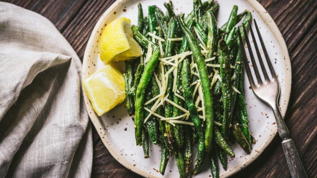 Green beans topped with shredded cheese and lemon wedges.