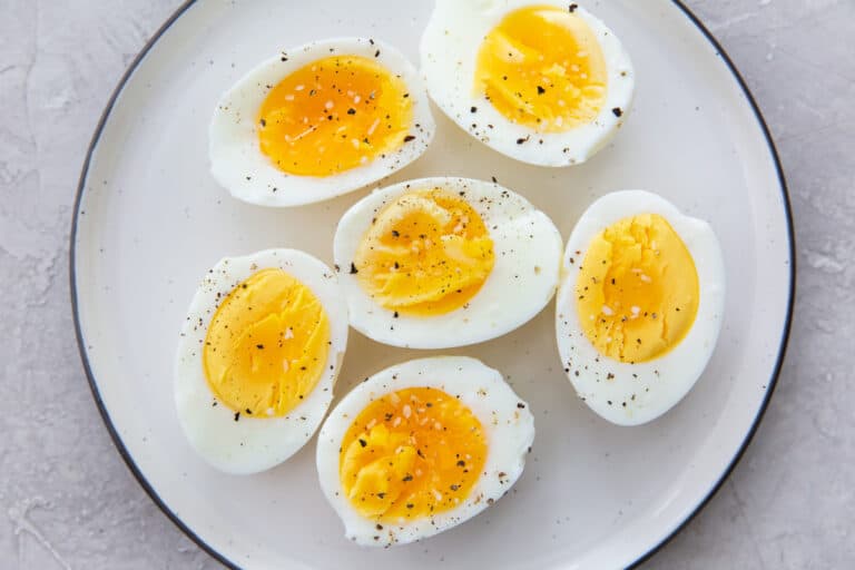 Plate with six halves of hard-boiled eggs, seasoned with black pepper, viewed from above on a light gray surface. Ideal for low carb diets.