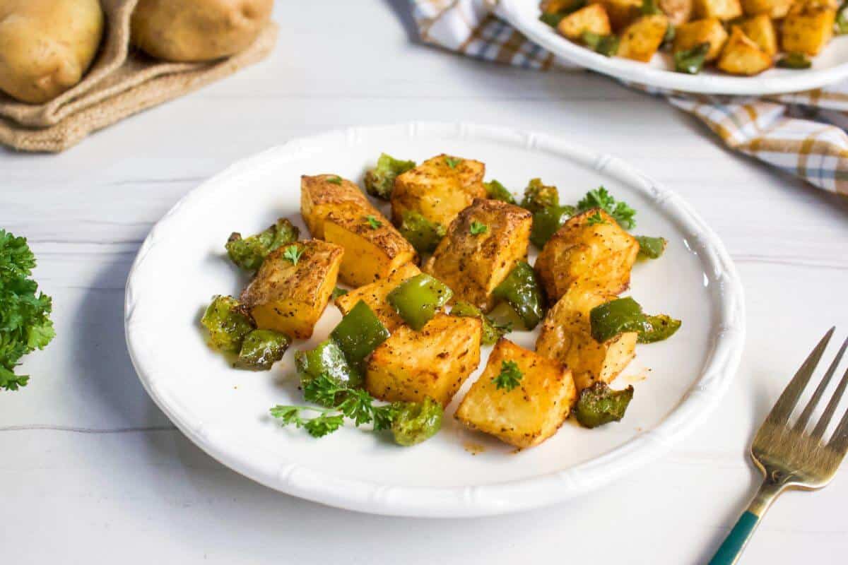Air-fried potato cubes with diced green bell peppers on plate.