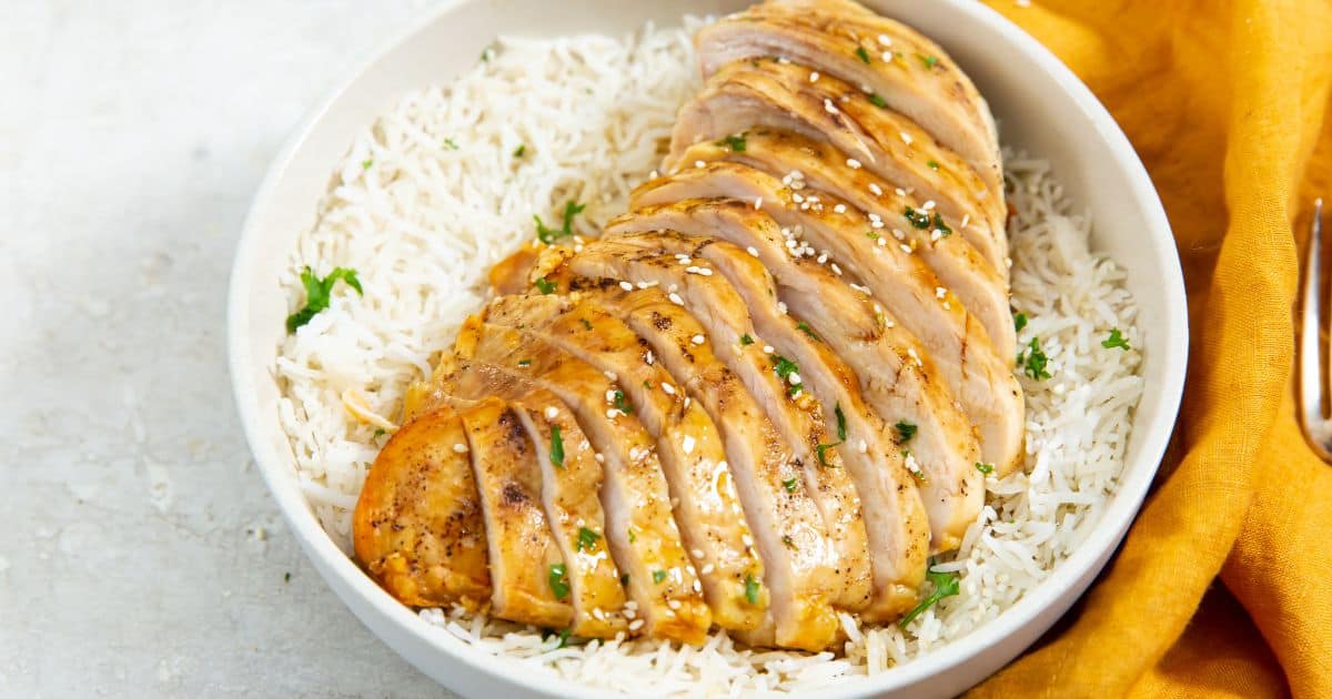 Easy Air Fryer Honey Chicken Breast in a white bowl with white rice, parsley, sesame seeds, and a fork.