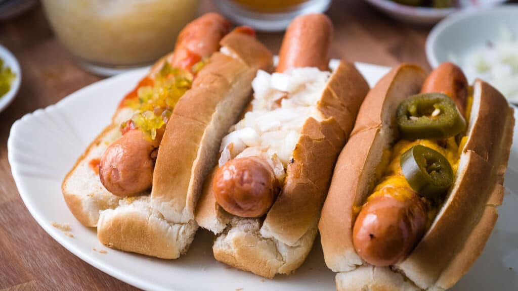 three air fryer hot dogs in buns with toppings.