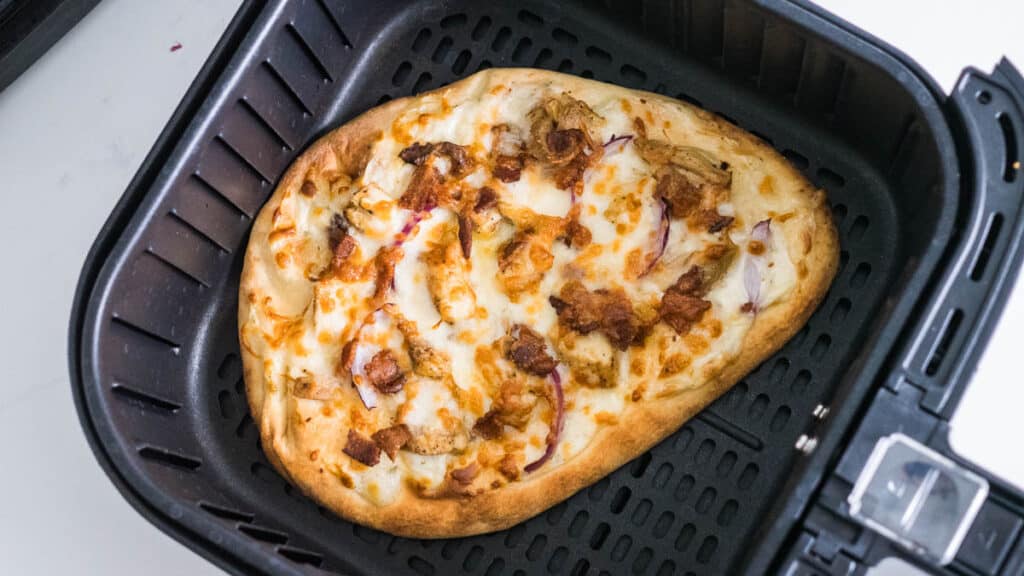 Naan pizza with chicken and bacon in the basket of an air fryer.
