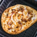 Naan pizza with chicken and bacon in the basket of an air fryer.