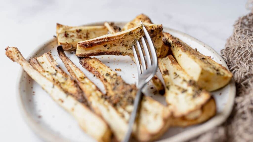 A fork stuck in a slice of parsnip dusted with dried herbs.