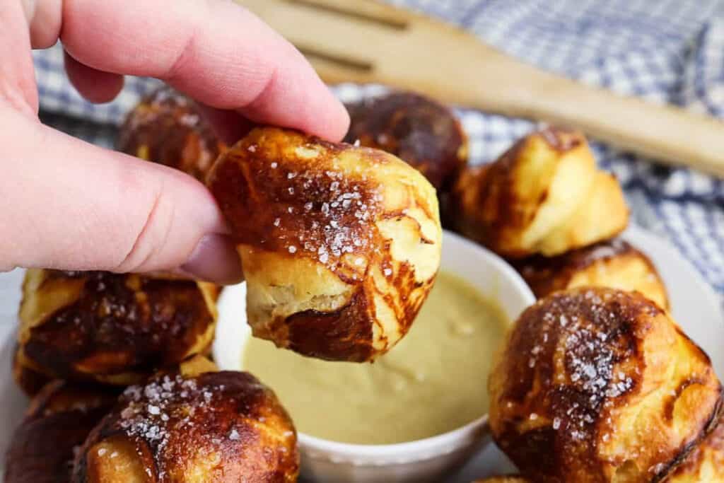 closeup of someone dipping a pretzel bite in mustard sauce.