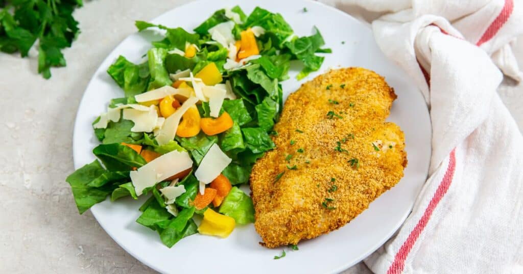 air fryer shake and bake chicken breast on a white plate with a side salad.