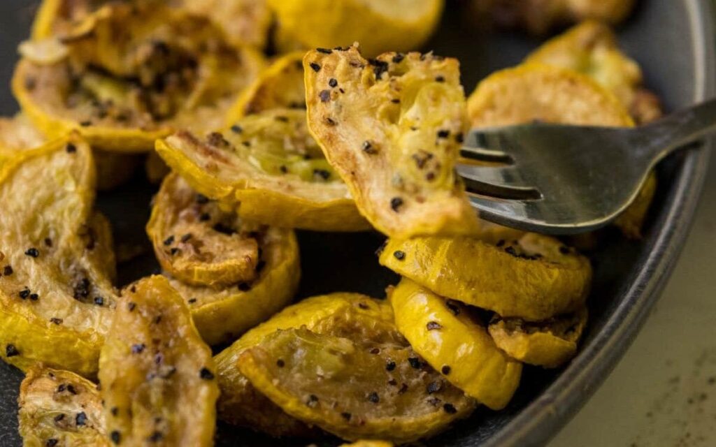 Air fryer yellow squash on a fork with more squash pieces in the background on a plate.