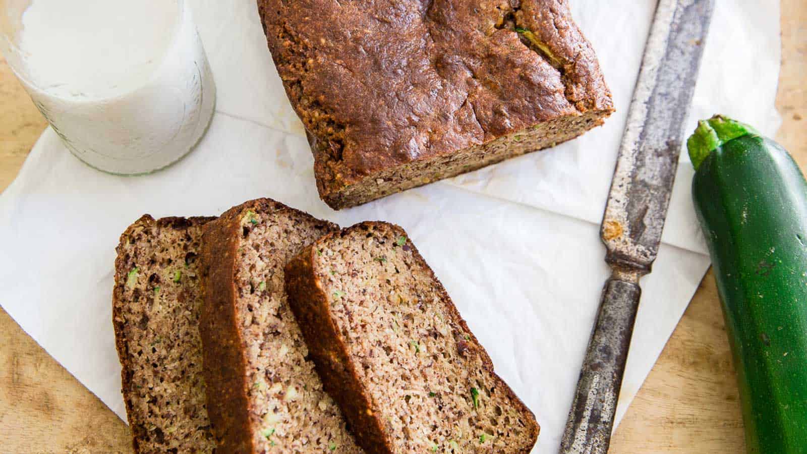 Paleo almond zucchini bread cut into slices with jug of milk, knife and zucchini to the side.