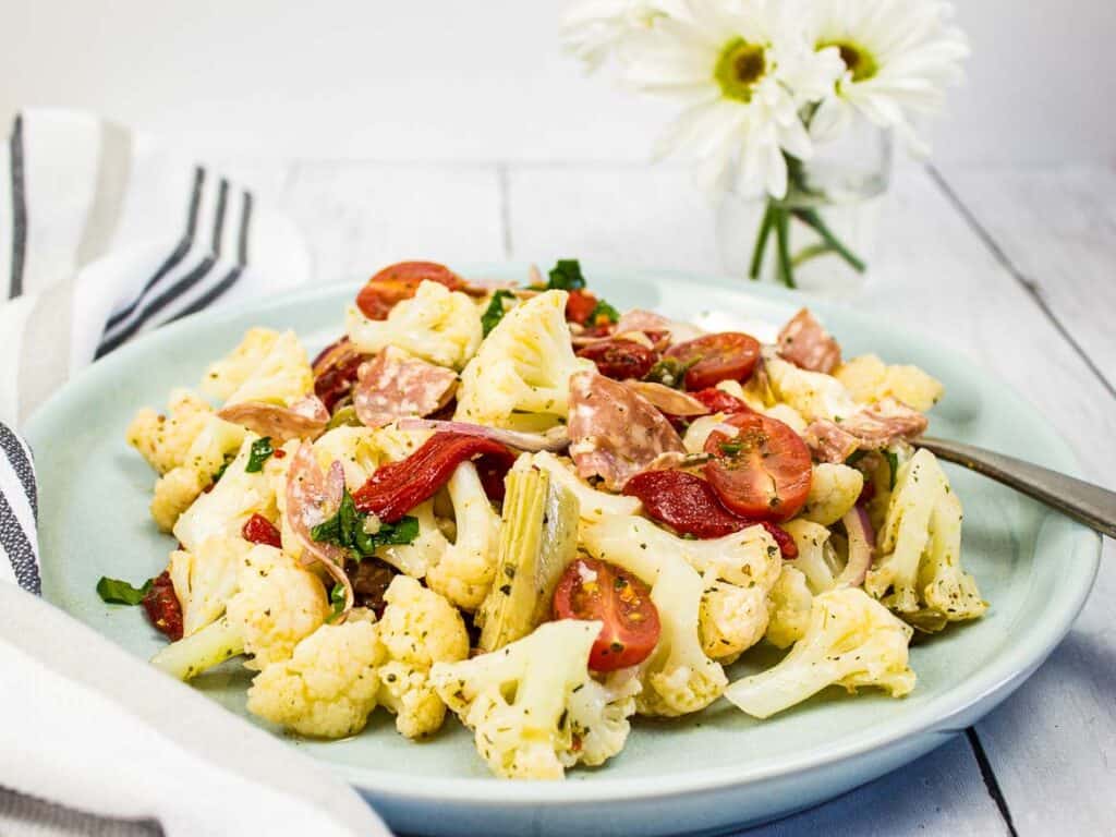 Low-carb Antipasto Salad on a round plate with daisies in the background.