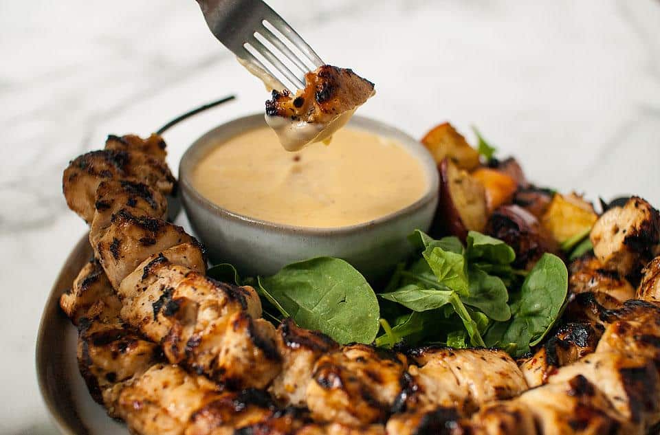 A fork dipping chicken from a skewer into dip.